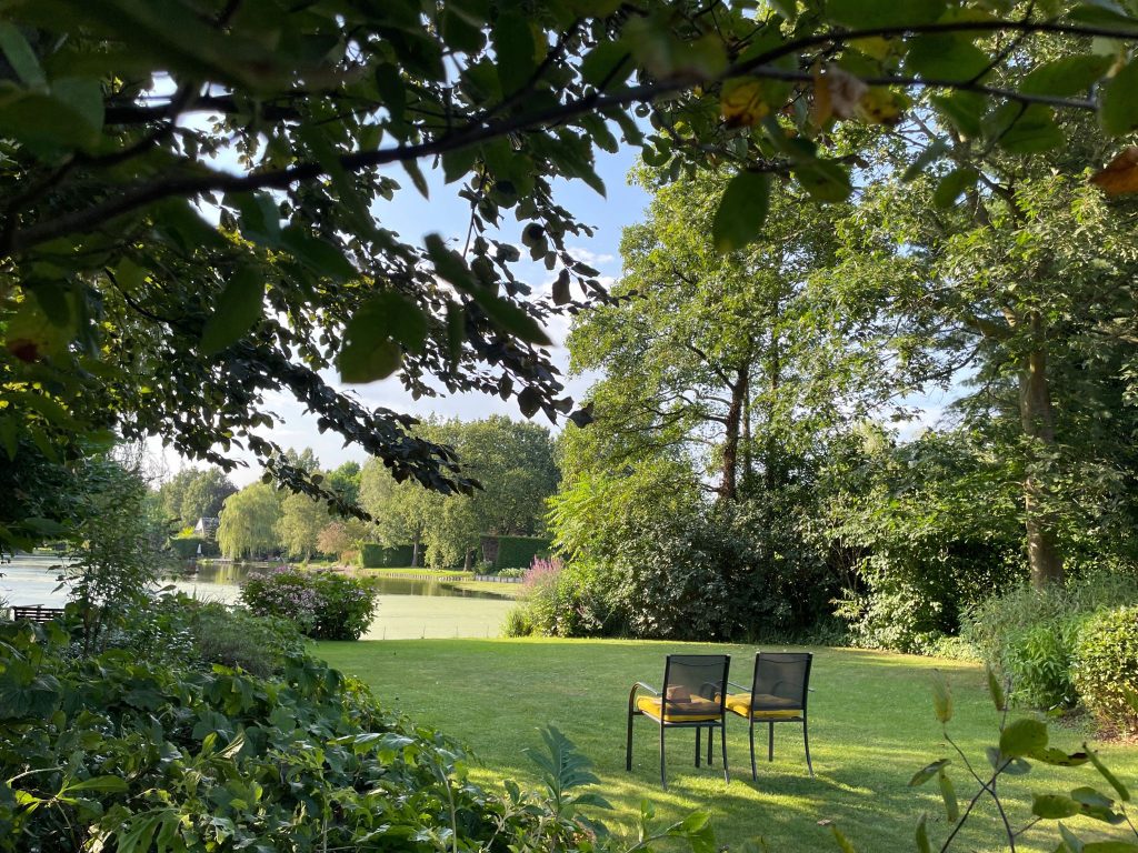 Twee stoelen op het gras onder de bomen, met de vijver op de achtergrond, in de tuin van Doyo