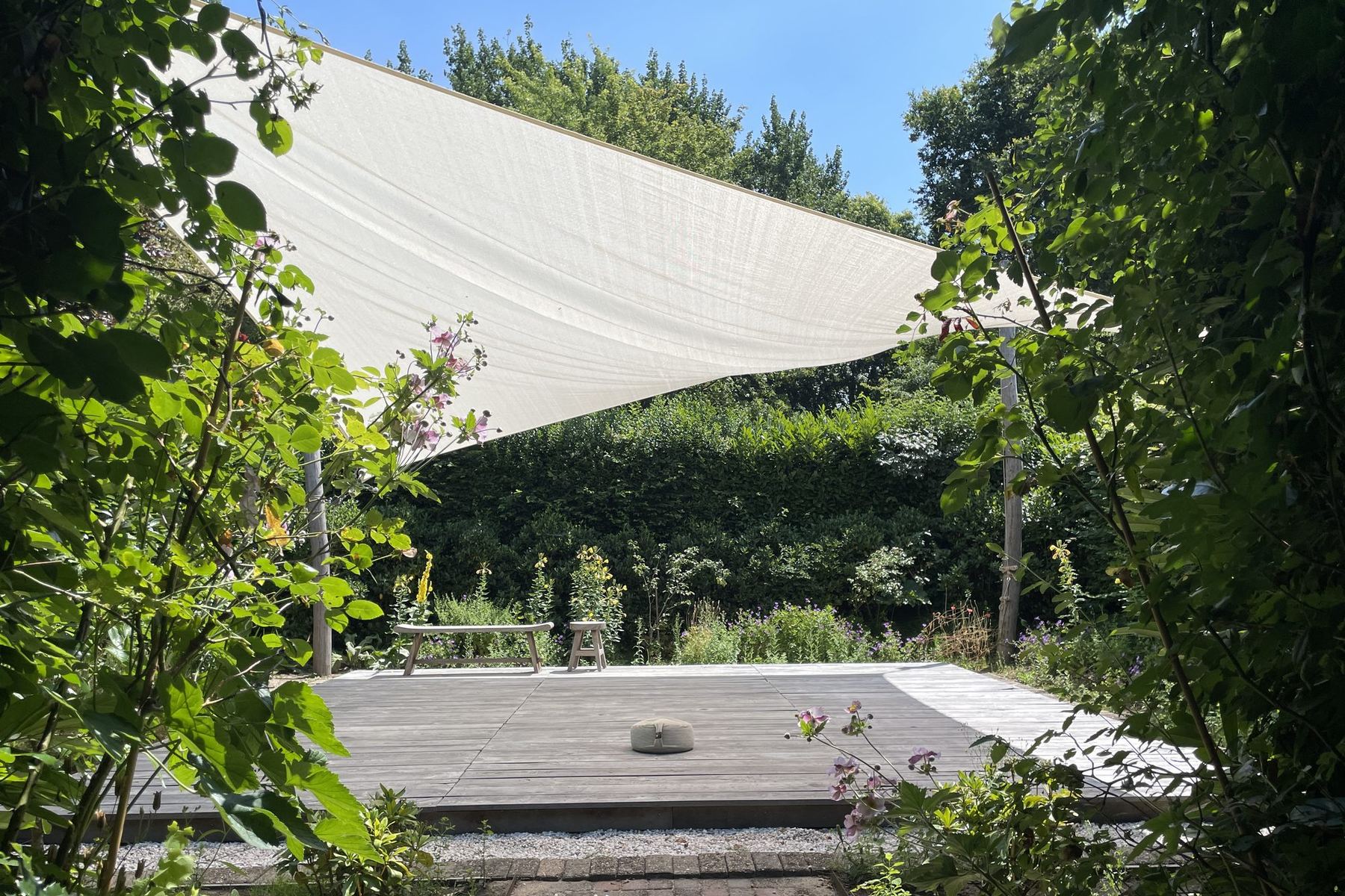 Lege buiten-dojo van Doyo Trainingen onder een wit schaduwzeil, met een meditatiekussen op het houten plateau en groen rondom