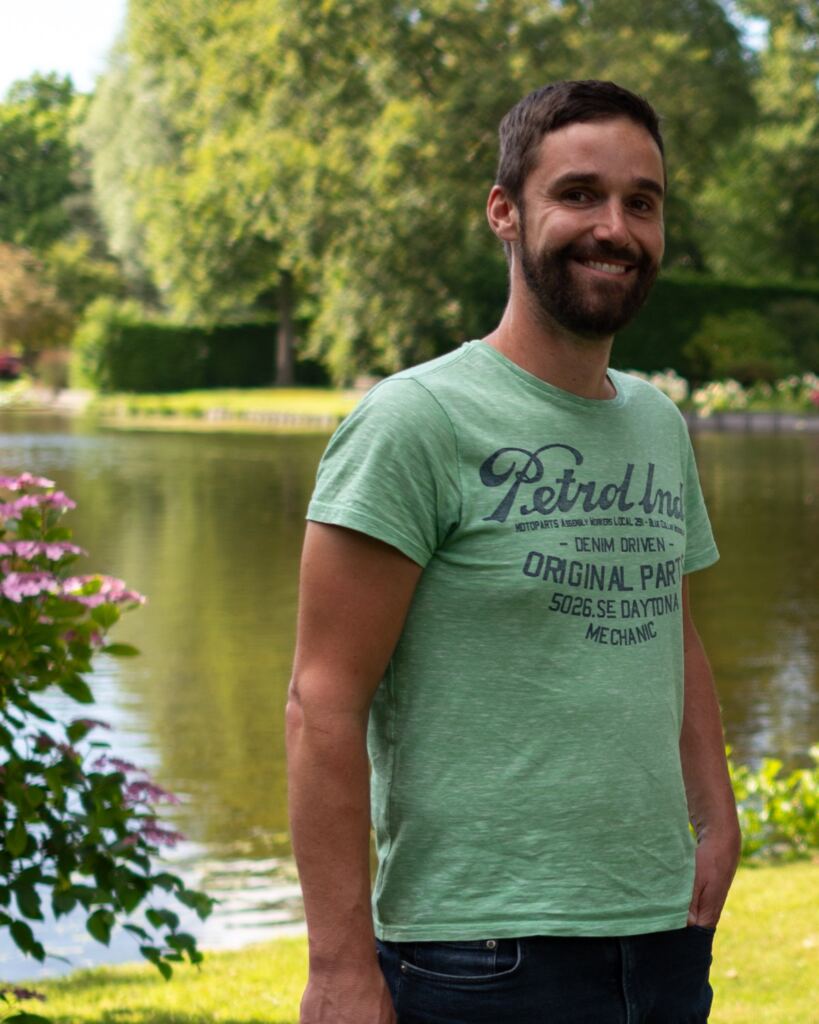 Michiel Bominaar, trainer van het Programma Zelfontwikkeling, staat lachend in de tuin van Doyo met de vijver achter zich
