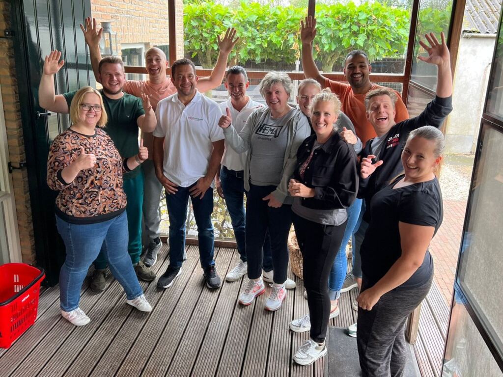 Een team van HEMA zwaait en lacht na afloop van hun TeamDag, samen met de trainers van Doyo